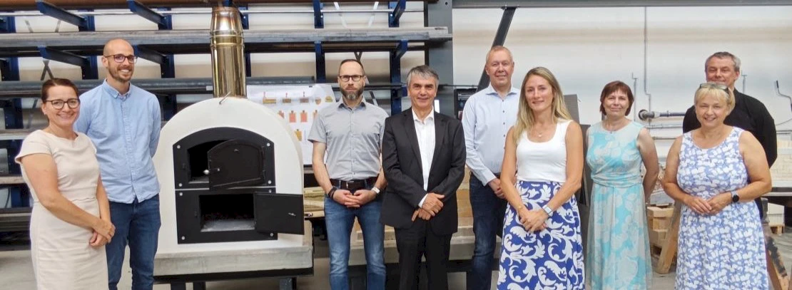 Group photo of the visitors from the Environmental Alliance and the State Secretary in the workshop hall next to a wood-fired oven